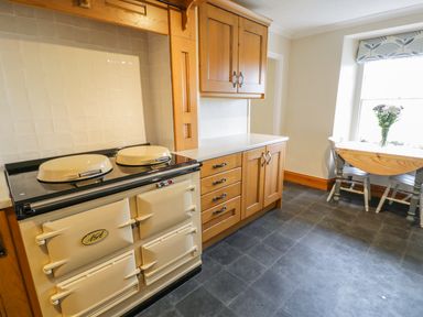 A kitchen with an aga stove wooden cabinets a table with chairs and a vase of flowers at Llety Perygl in Harlech