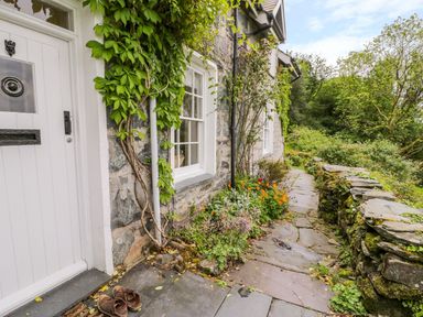 A stone pathway with plants and flowers beside a stone house with white door and windows at Llety Perygl in Harlech