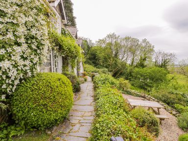 A stone pathway along a house with flowering plants and shrubs next to a wooden picnic table in a garden at Llety Perygl in Harlech