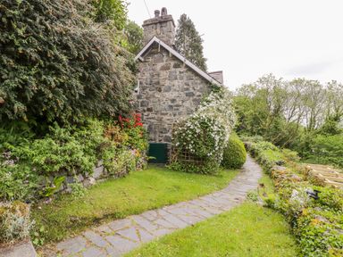 A stone house beside a garden path with bushes and flowers along the path at Llety Perygl in Harlech