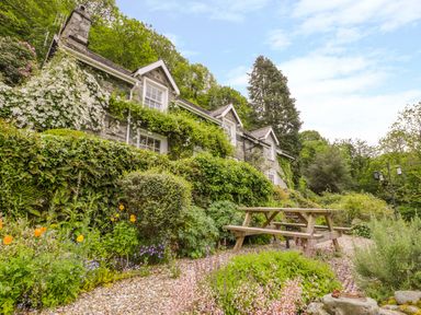 An outdoor garden area with a wooden picnic table and a stone house covered in plants at Llety Perygl in Harlech