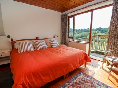 A bedroom with a double bed red bedding striped pillows bedside tables sliding glass door and balcony overlooking trees at Plasybangor in Newport Pembrokeshire