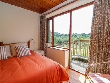 A bedroom with an orange bedspread striped pillows wooden ceiling and a large window overlooking greenery at Plasybangor Newport Pembrokeshire