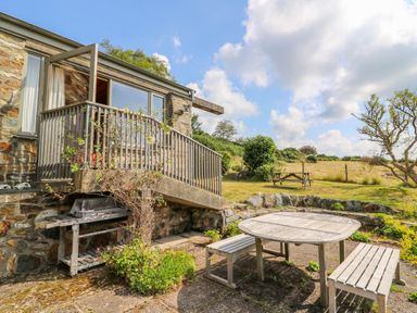 An outdoor patio area with a wooden table and benches near a stone building at Plasybangor in Newport Pembrokeshire