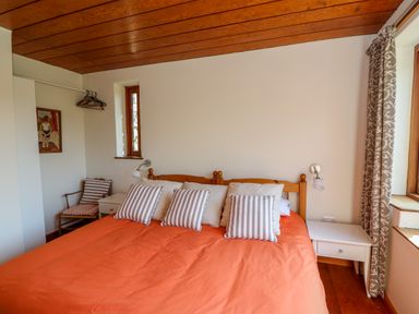 A bedroom with an orange bedspread a wooden bed frame striped pillows bedside tables with lamps and a wooden chair at Plasybangor in Newport Pembrokeshire