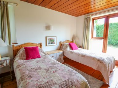 A bedroom with two single beds with pink pillows and quilts a small dresser a lamp a framed picture on the wall and a window with curtains at Plasybangor in Newport Pembrokeshire