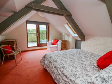 A bedroom with a bed with patterned bedding a white armchair a wicker chair a wooden chest of drawers and a balcony door at Plasybangor in Newport Pembrokeshire