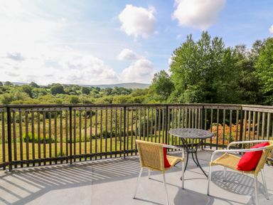 A balcony with two chairs and a round table overlooking trees and fields at Plasybangor in Newport Pembrokeshire