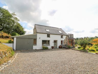 A white house with a garage and gravel driveway surrounded by trees and garden at Plasybangor Newport Pembrokeshire