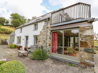 Exterior view of a stone and white plaster cottage with patio furniture and upper balcony at Plasybangor in Newport Pembrokeshire