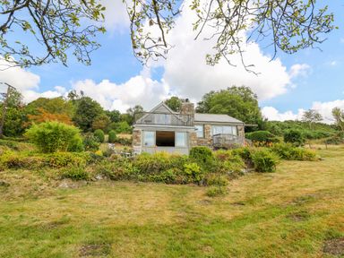 A stone house with a garden and lawn surrounded by trees at Plasybangor in Newport Pembrokeshire