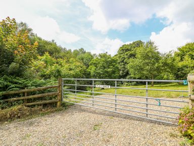 A metal gate with a sign on a gravel driveway leading to a grassy area with trees at Plasybangor in Newport Pembrokeshire