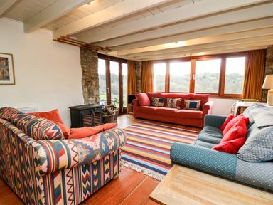 A living room with three sofas a striped rug a wood stove and large windows at Plasybangor in Newport Pembrokeshire