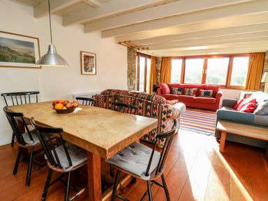 A living room with a wooden dining table and black chairs and sofas with patterned cushions at Plasybangor in Newport Pembrokeshire