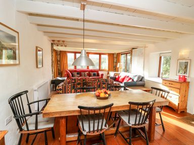 A dining area with a wooden table and black chairs next to a living room with sofas and windows at Plasybangor in Newport Pembrokeshire