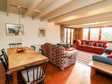 A living room with patterned sofas a red couch wooden dining table with black chairs and large windows at Plasybangor in Newport Pembrokeshire