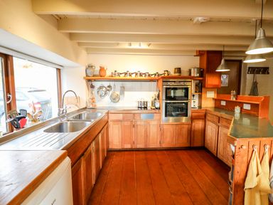 A kitchen with wooden cabinets double sinks pots and pans on counters and hanging utensils at Plasybangor in Newport Pembrokeshire