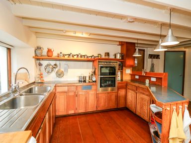 A kitchen with wooden cabinets stainless steel sink pots on a shelf and hanging utensils at Plasybangor in Newport Pembrokeshire