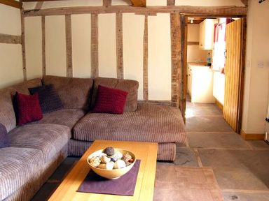 A living room with a brown sectional sofa a wooden coffee table with a bowl of decorative balls and exposed wooden beams on walls at Point Cottage in Preston-on-Wye near Hereford