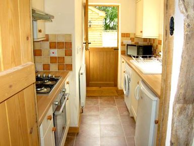 A narrow kitchen with stove oven microwave washing machine and sink at Point Cottage Preston on Wye near Hereford