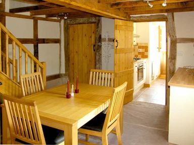 A dining area with a wooden table and chairs next to a staircase and a kitchen door at Point Cottage in Preston-on-Wye near Hereford
