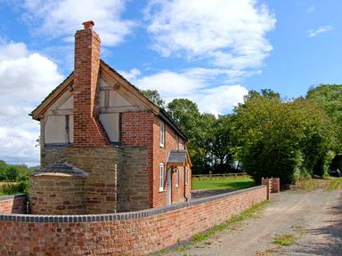 A brick and stone cottage with a chimney and a low brick wall beside a gravel path at Point Cottage in Preston-on-Wye near Hereford