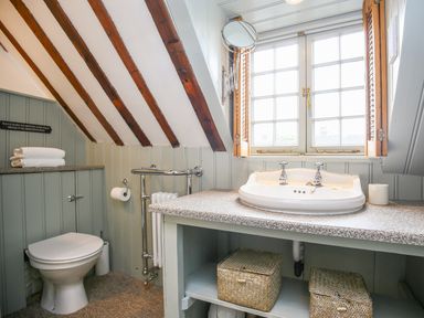A bathroom with a toilet, sink, towels, window, and wicker baskets at Murton Cottage in Burford