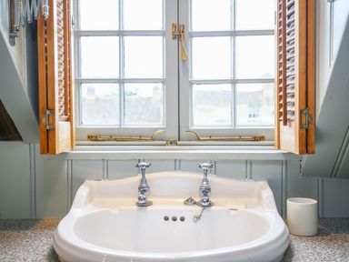 A bathroom sink with two faucets under a window with wooden shutters at Murton Cottage in Burford