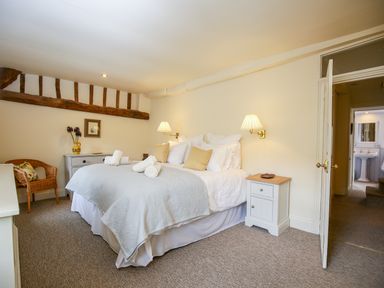 A bedroom with a double bed side tables wicker chair and bathroom visible through an open door at Murton Cottage in Burford