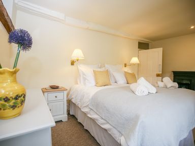 A bedroom with a bed with white linens and yellow pillows with rolled towels on top at Murton Cottage in Burford