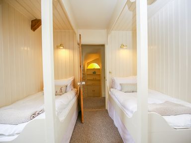 A bedroom with two single beds with wall lights and a wooden door leading to a lit alcove with shelves at Murton Cottage in Burford