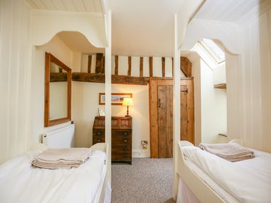 A bedroom with two single beds a wooden dresser a mirror wooden door and exposed wooden beams at Murton Cottage in Burford