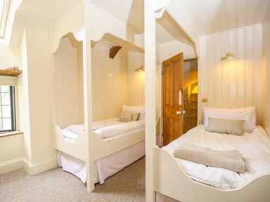 A small bedroom with two single beds each framed with white wood and a wooden door at Murton Cottage in Burford