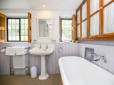 A bathroom with a white pedestal sink a bathtub a towel radiator and wooden cabinets at Murton Cottage in Burford