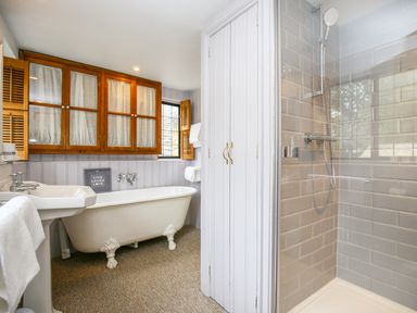 A bathroom with a clawfoot bathtub sink wooden cabinets and a tiled walk-in shower at Murton Cottage in Burford