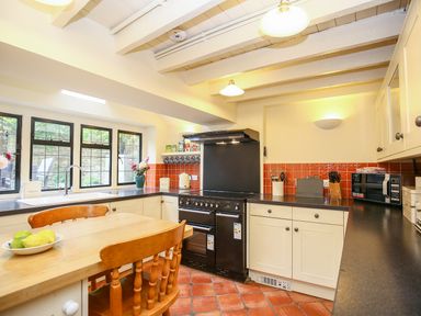 A kitchen with cream cabinets black countertops a black stove a wooden table and chairs and a window with multiple panes at Murton Cottage in Burford