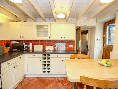 A kitchen with white cabinets red tiled backsplash wooden table and chairs at Murton Cottage in Burford