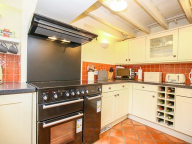 A kitchen with cream cabinets black countertop black oven and stove orange tile backsplash and a wine rack at Murton Cottage in Burford