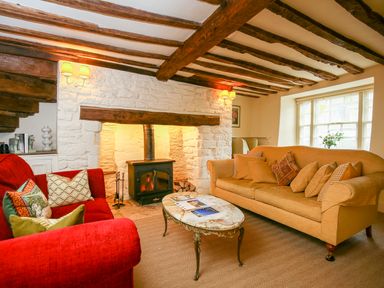 A sitting room with exposed wooden beams a stone fireplace two sofas and a coffee table at Murton Cottage in Burford