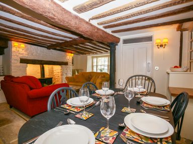 A dining table set with plates and glasses in a living room with exposed wooden beams and sofas at Murton Cottage in Burford