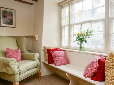 A sitting area with a green armchair and a window bench with red and yellow cushions and a vase of flowers at Murton Cottage in Burford