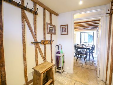 A hallway with wooden hooks bench and umbrella stand leading to a dining area at Murton Cottage in Burford