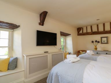 A bedroom with two single beds folded towels on bed a wall mounted TV and wooden beams at Murton Cottage in Burford