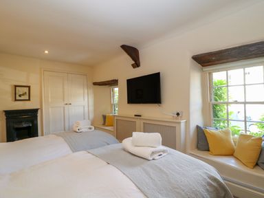 A bedroom with two beds stacked towels a wall mounted television window seats with cushions and a built in wardrobe at Murton Cottage in Burford