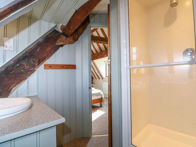 A bathroom with a sink and shower next to a doorway leading to a bedroom with visible wooden beams at Murton Cottage in Burford