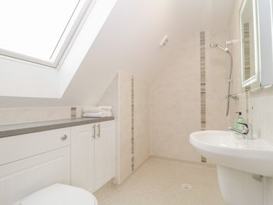 A bathroom with a white sink a shower head a cabinet with towels and a skylight window at The Forge in Shipham