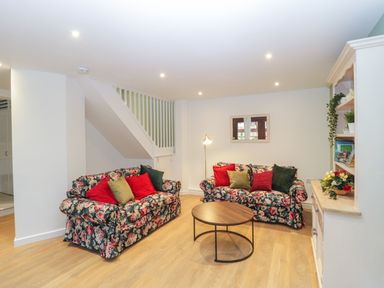 A living room with floral sofas red and green pillows a round wooden coffee table and a white shelving unit at The Forge in Shipham