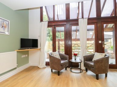 A sitting area with two armchairs and a small round table between them in front of large wooden framed glass doors at The Forge in Shipham