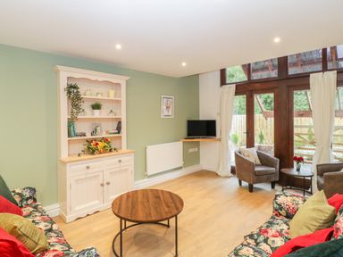 A living room with floral sofas a wooden coffee table a white cabinet and glass doors at The Forge in Shipham