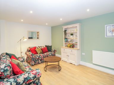 A living room with floral sofas red and green cushions a round wooden coffee table a white cabinet and green walls at The Forge in Shipham